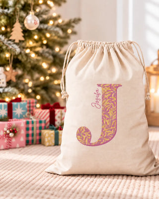 Saco de Navidad personalizado con inicial y nombre junto a un árbol de Navidad